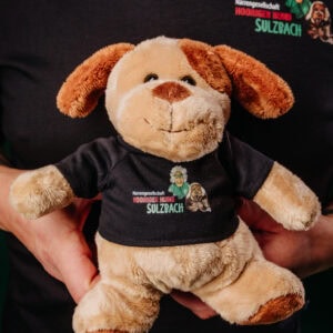 Hooriger Hund Plüschtier, weiches Stofftier, Sammelobjekt, ideal für Hunde-Fans, personalisiertes Souvenir oder Geschenk, mitten in einer schwarzen T-Shirt mit Logo von Hooriger Hund Sulzbach.