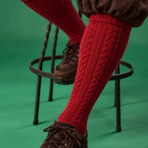 Rote, handgestrickte Socken mit Kabelmuster, getragen von einer Person im Sitzen auf einem Stuhl.